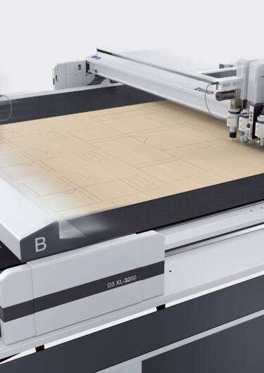 Zünd D3 XL-3200 digital cutter with multiple moving heads precisely cutting patterns on a light brown material. Zünd D3 XL-3200 digital cutter with multiple moving heads precisely cutting patterns on a light brown material.