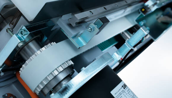 Close-up view of the direct drive mechanism within a Zünd cutting system, showcasing gears, belts, and a spring. Close-up view of the direct drive mechanism within a Zünd cutting system, showcasing gears, belts, and a spring.