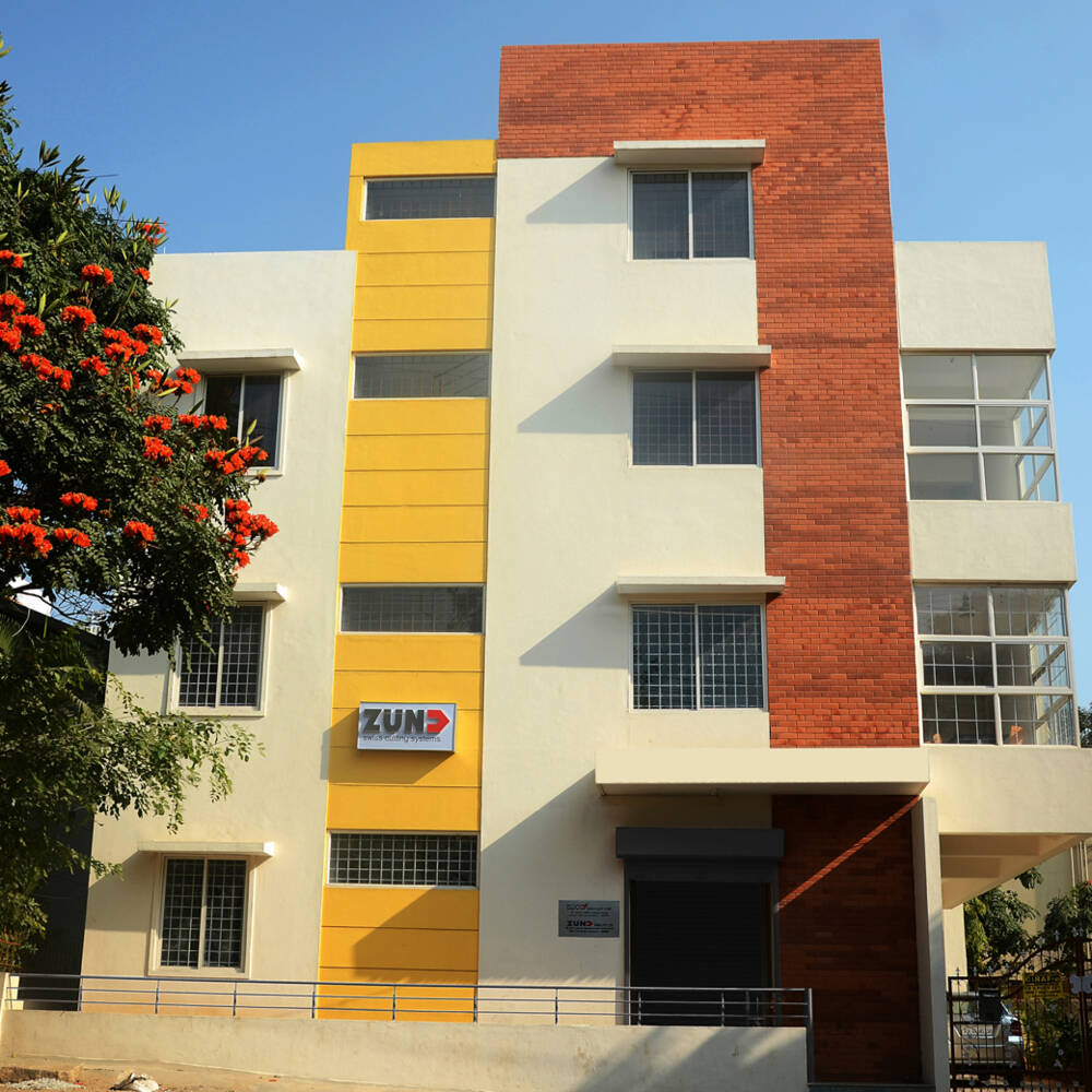 Moderne ZIN-gebouw met bakstenen accenten, gele panelen en opvallende oranje bloeiende takken aan de linkerkant. Moderne ZIN-gebouw met bakstenen accenten, gele panelen en opvallende oranje bloeiende takken aan de linkerkant.