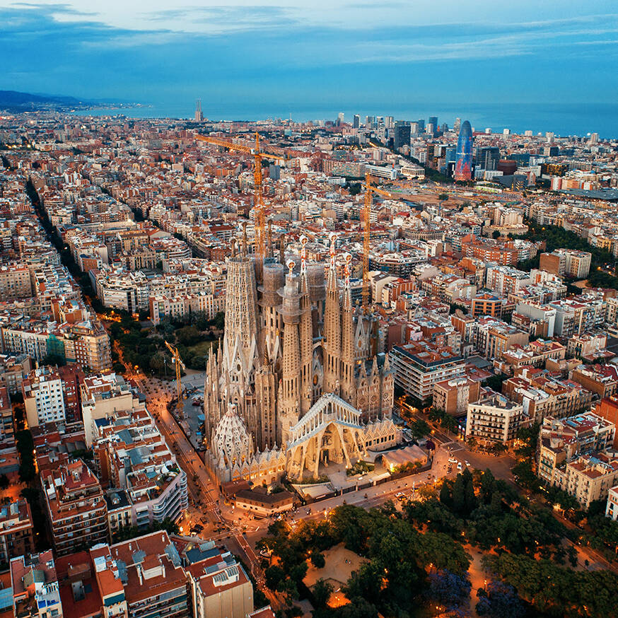 Luftaufnahme Barcelona Aerial view of Barcelona, Spain, showcasing the Sagrada Familia basilica and surrounding cityscape at dusk, with cranes indicating ongoing construction.