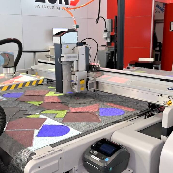 Sistema de corte Zünd con brazo robótico procesando material con patrones de colores y líneas de proyección. Sistema de corte Zünd con brazo robótico procesando material con patrones de colores y líneas de proyección.