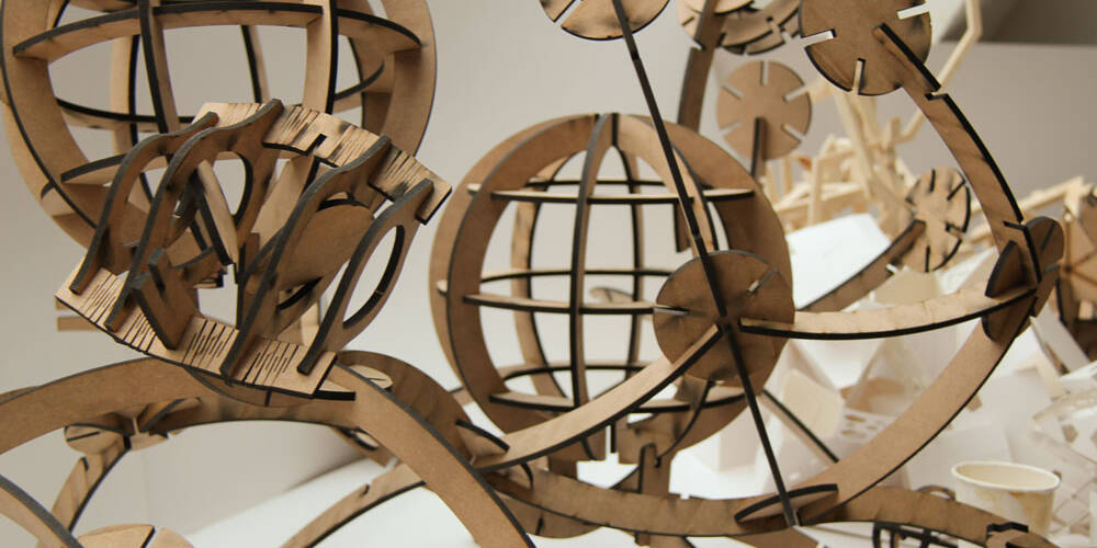Abstract architectural model made of laser-cut wood, resembling interconnected spherical structures with geometric elements.