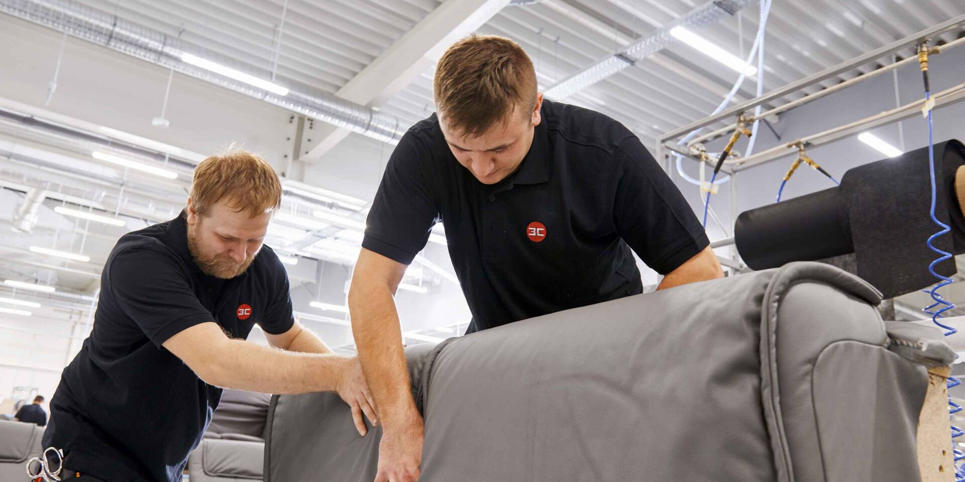 Due operai con polo nere con logo 3C lavorano su un rivestimento grigio in un'officina.