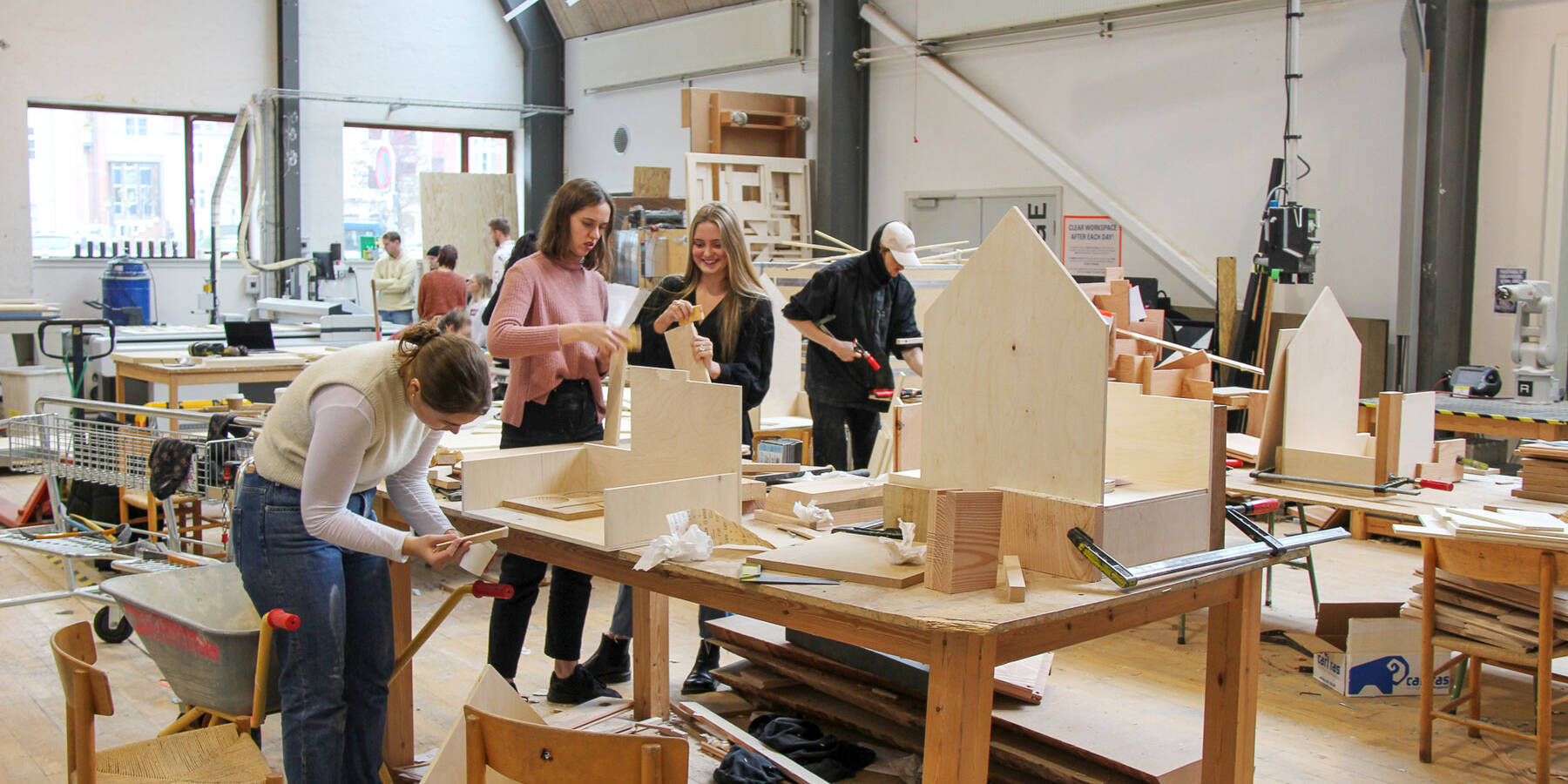 Students work on wooden architectural models in a workshop at Aarhus Architecture School, utilizing various tools and materials for their projects.