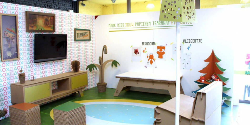 Een speelse, kindvriendelijke display met kartonnen meubels, decoraties en muurkunst, inclusief een tv en zitjes.