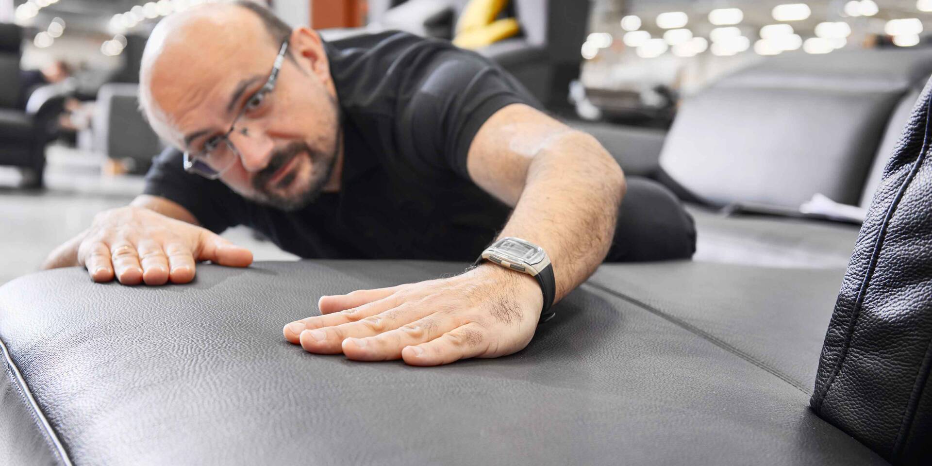 Un uomo con occhiali si sdraia su un divano di pelle grigia, esaminando attentamente la superficie.