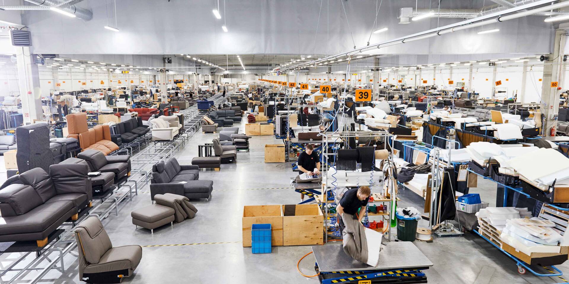 Fabbrica di mobili con operai che lavorano su divani e componenti, con Zünd Systemtechnik in evidenza.