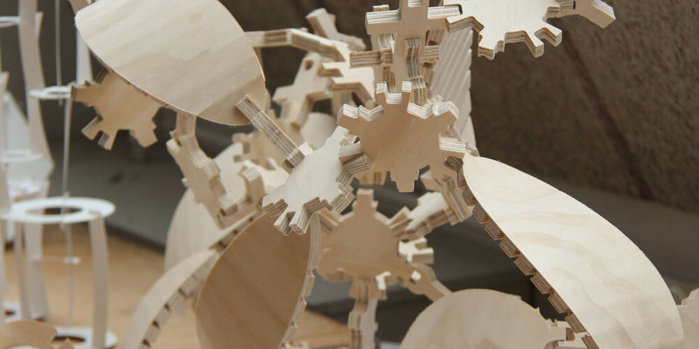 Close-up of a complex wooden gear mechanism, showcasing intricate interlocking parts and layered plywood construction.