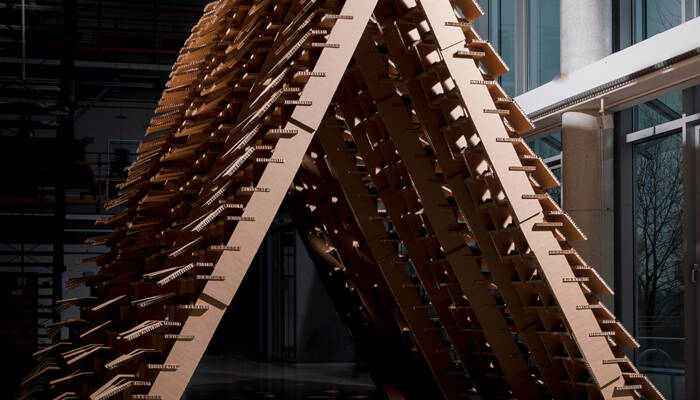 Struttura architettonica a forma di tenda, realizzata con pannelli di cartone tagliati con precisione, in un ambiente interno. Struttura architettonica a forma di tenda, realizzata con pannelli di cartone tagliati con precisione, in un ambiente interno.