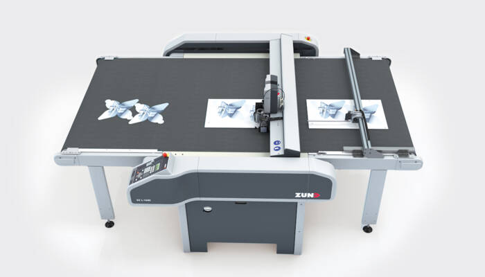 Máquina de corte Zünd S3 L-1600 cortando formas em papel, com duas borboletas já cortadas na mesa. Máquina de corte Zünd S3 L-1600 cortando formas em papel, com duas borboletas já cortadas na mesa.