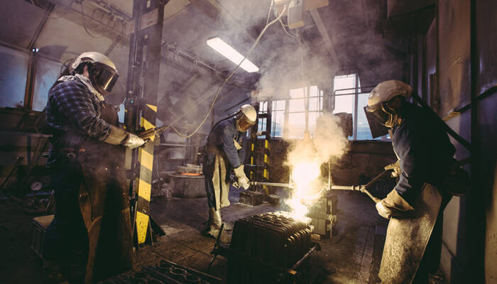 Arbeiders in beschermende kleding gieten gesmolten metaal in een fabriek, met veel rookontwikkeling. Arbeiders in beschermende kleding gieten gesmolten metaal in een fabriek, met veel rookontwikkeling.