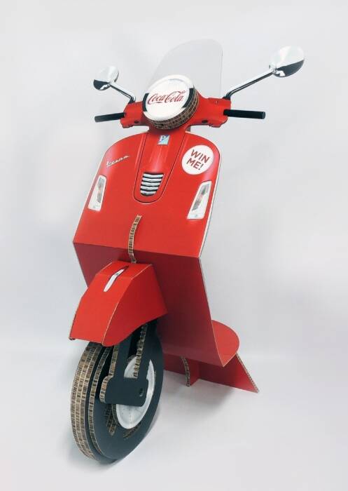 Rode kartonnen Vespa-scooter met Coca-Cola logo en 'Win Me!' sticker, geïsoleerd op witte achtergrond.