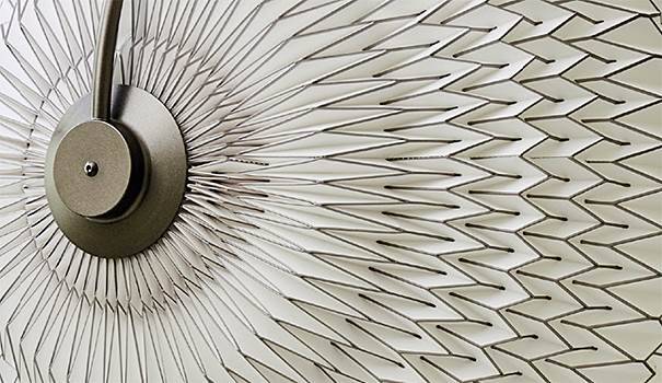 Close-up of a metallic circular object with radiating lines, creating a geometric pattern on a white textured surface. Close-up of a metallic circular object with radiating lines, creating a geometric pattern on a white textured surface.